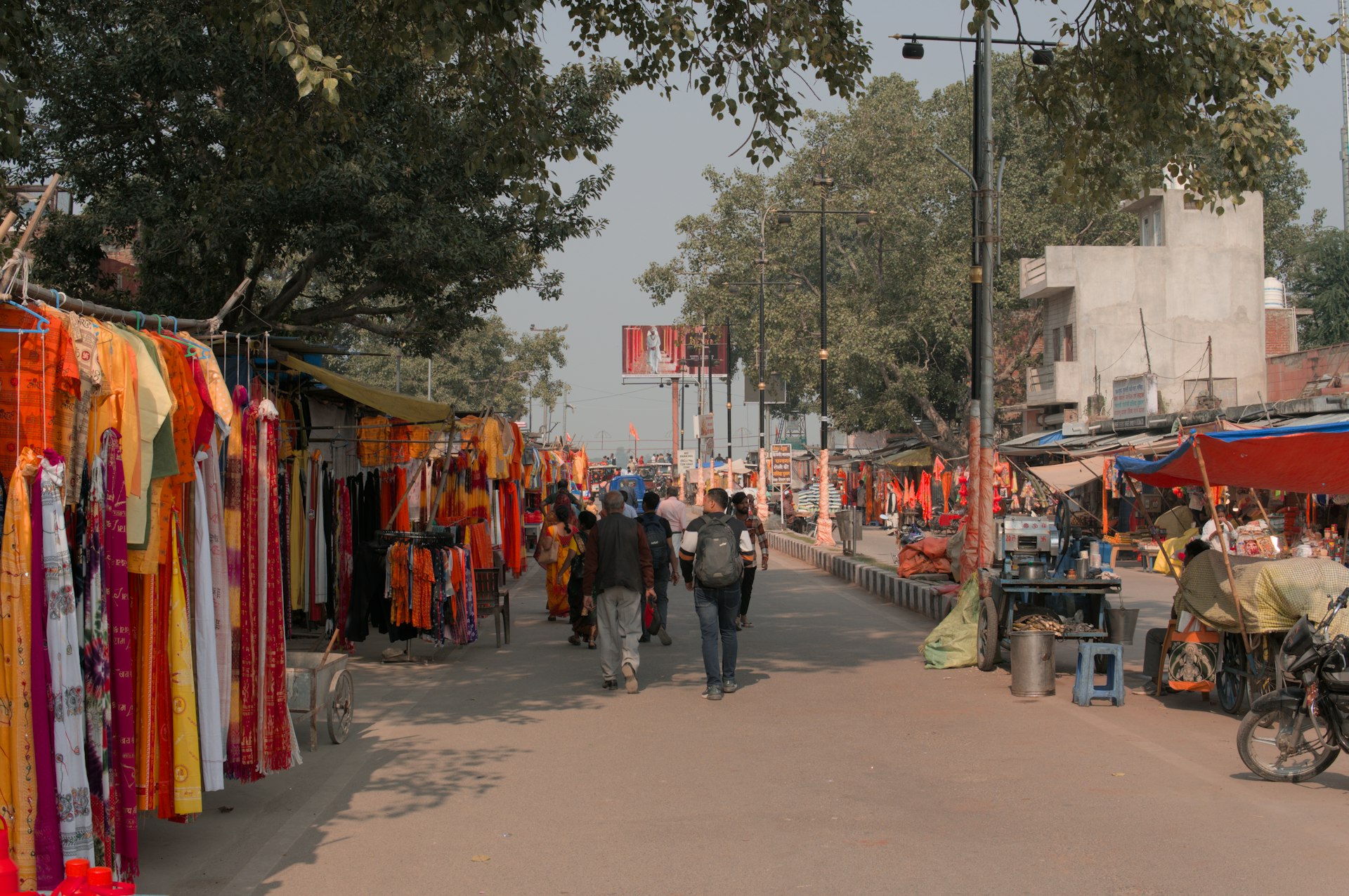 People walk along a street lined with colorful clothing stalls.